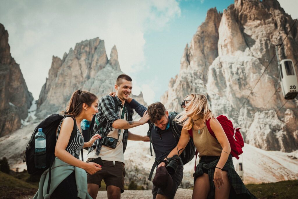 Fünf junge Menschen beim Wandern in den Bergen, lachen und helfen sich gegenseitig.