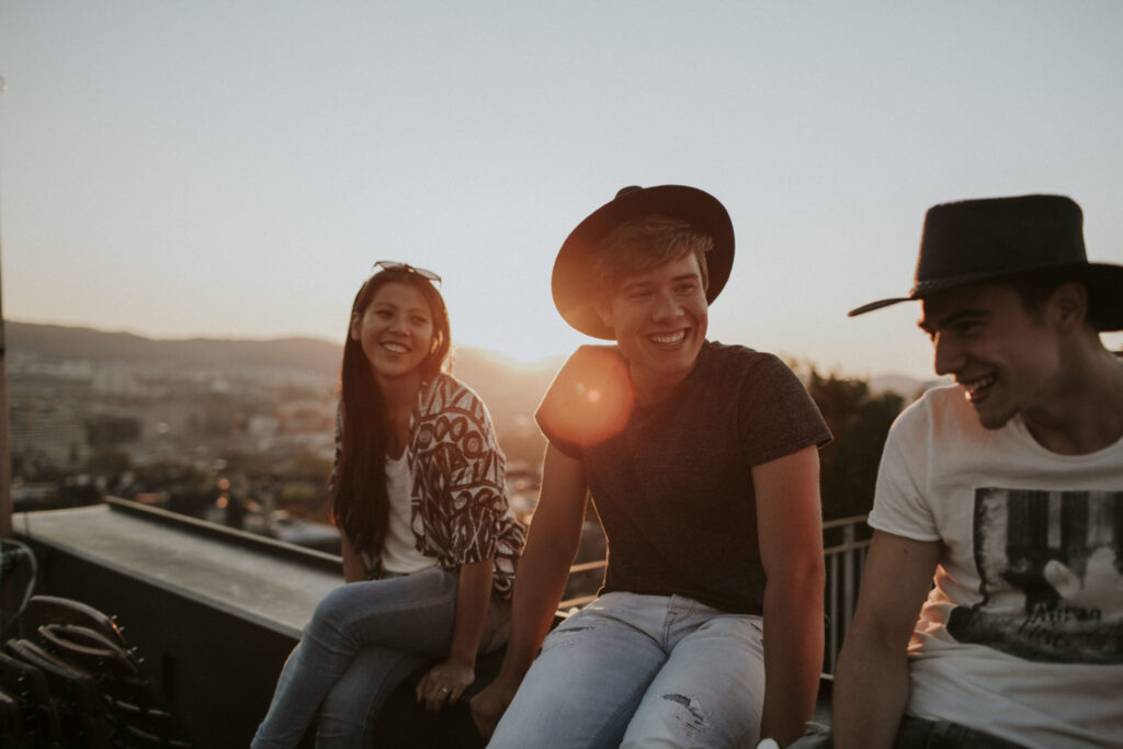 Drei junge Menschen sitzen auf einer Dachterrasse, lachen und unterhalten sich.
