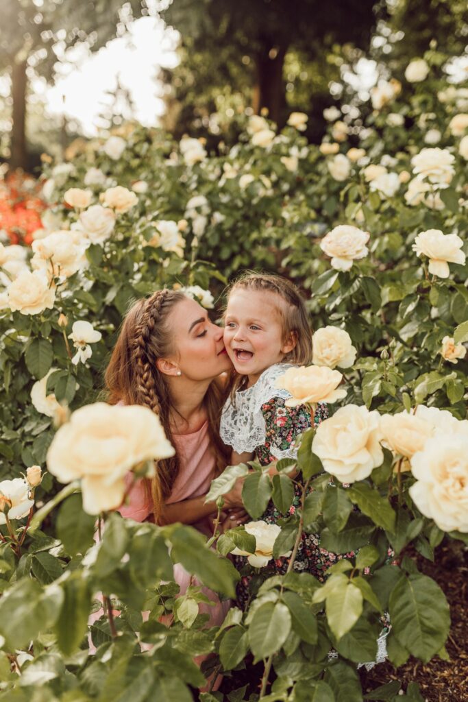 Mutter küsst lachendes Kind in einem Rosenbeet.