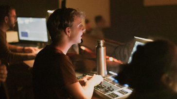Junge Menschen bei einem Online-Gottesdienst in Augsburg, die an Computern und Mischpulten arbeiten, um spirituelle Gemeinschaft digital zu erleben.