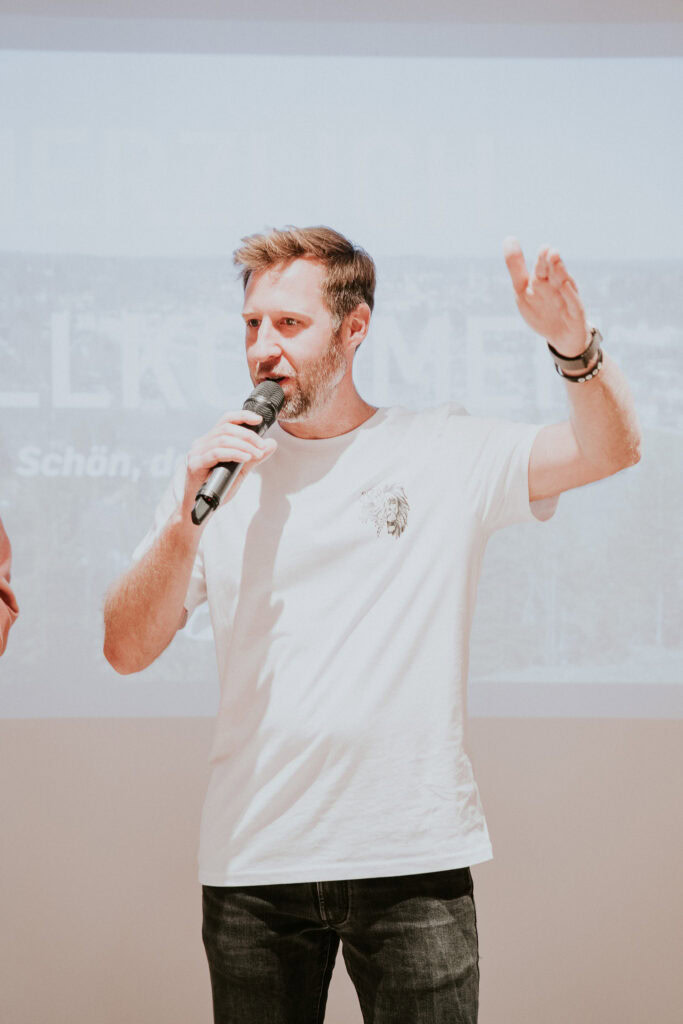 Mann mit Mikrofon spricht und hebt die Hand.