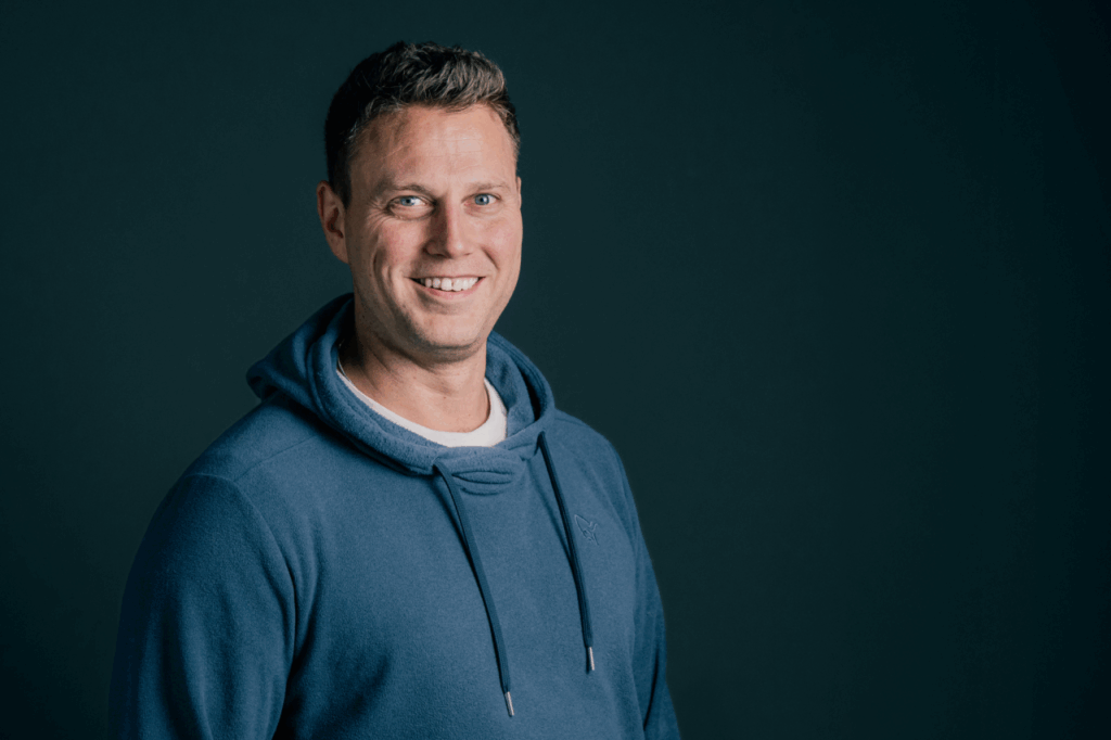 Freundlicher junger Mann in blauer Hoodie vor dunklem Hintergrund, repräsentiert die Gemeinschaft und den Glauben bei ICF Balingen.
