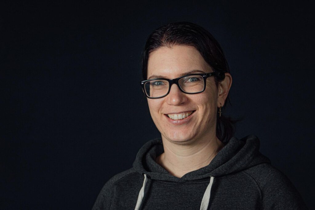 Lächelnde Frau mit Brille und dunklem Hoodie, die für die Gemeinde ICF Balingen steht, symbolisiert Gemeinschaft und Glauben.