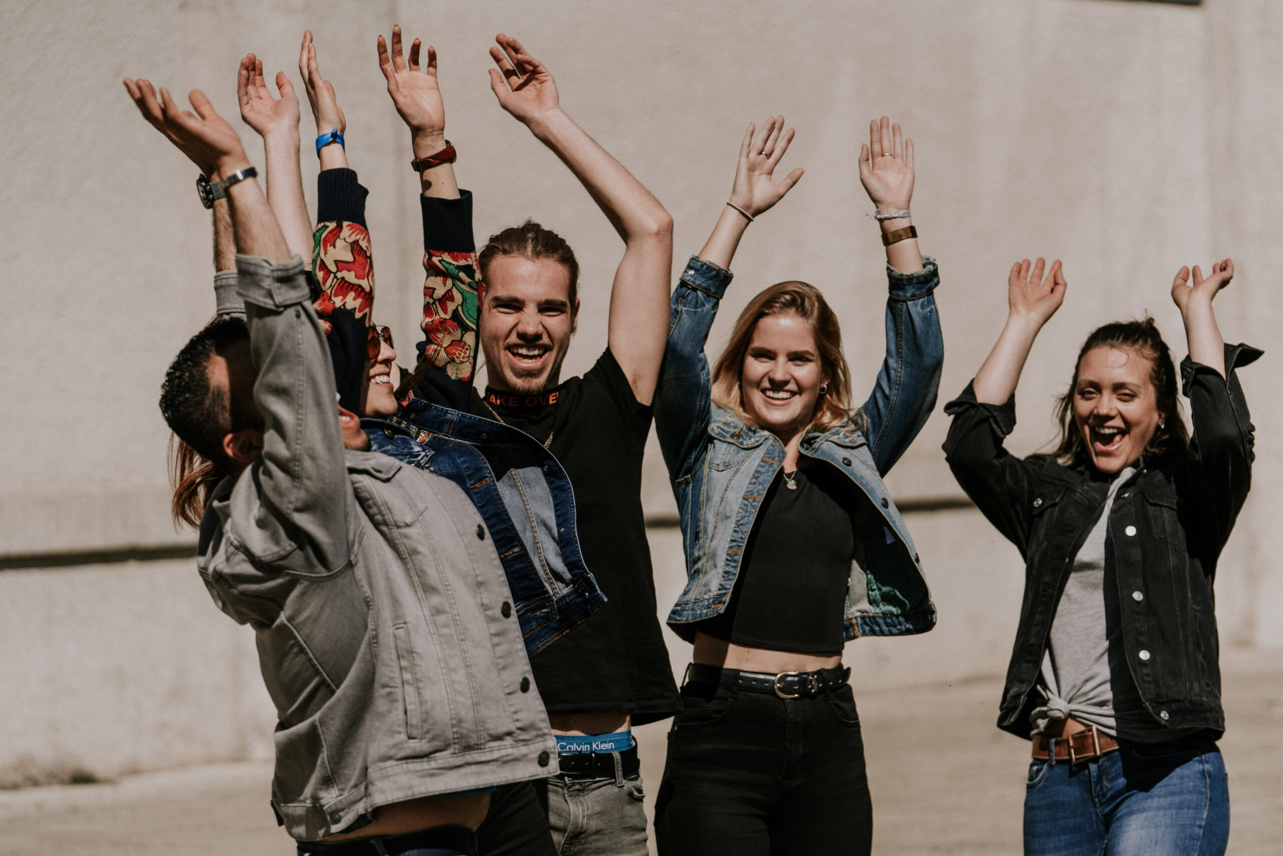 Vier junge Menschen mit erhobenen Armen, lachen und freuen sich.
