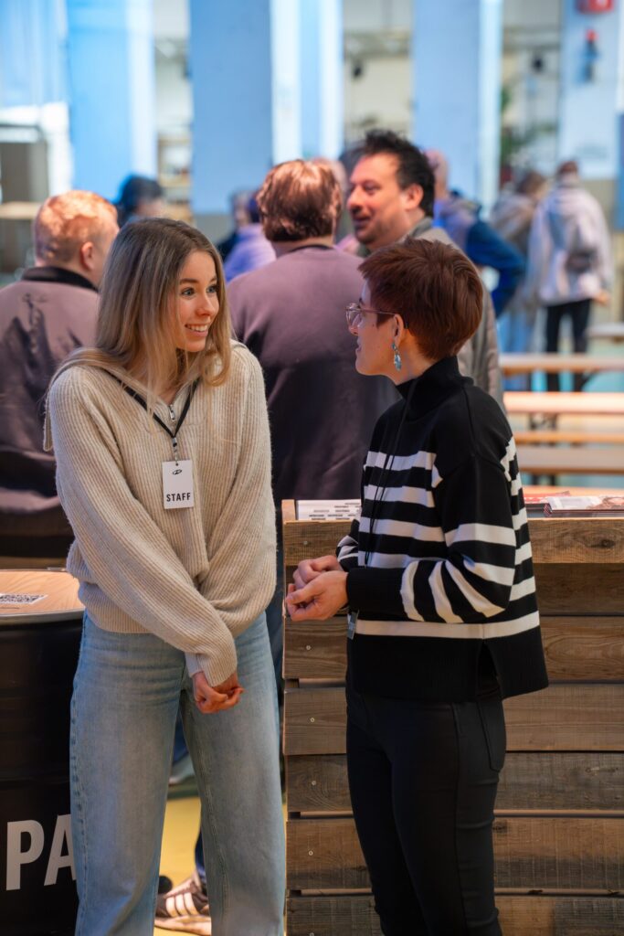 Zwei Frauen im Gespräch bei einer ICF-Veranstaltung in Basel, umgeben von weiteren Teilnehmern, die sich in einem modernen, hellen Raum austauschen.
