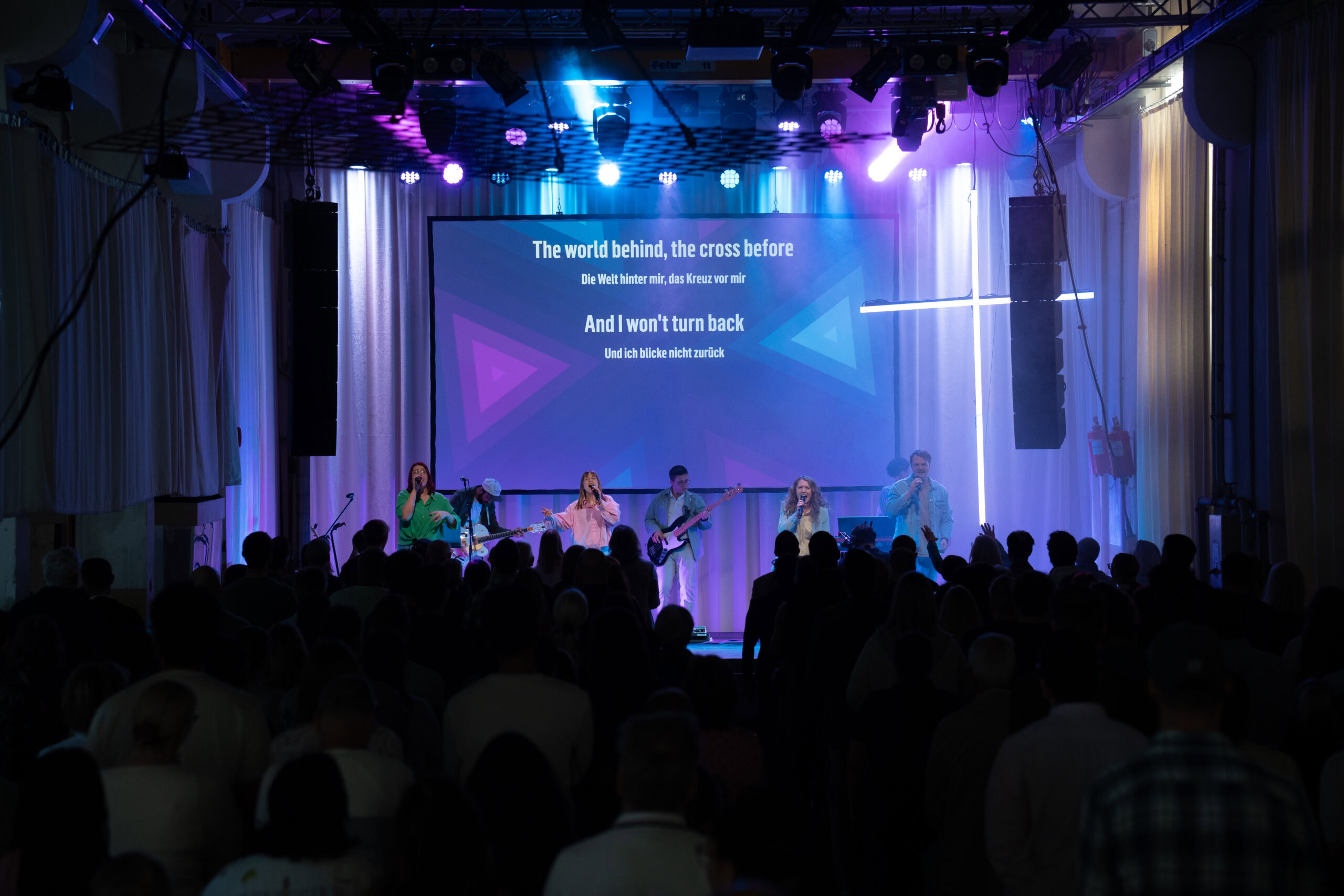 Musiker auf der Bühne mit Lichtshow und Publikum im Saal.