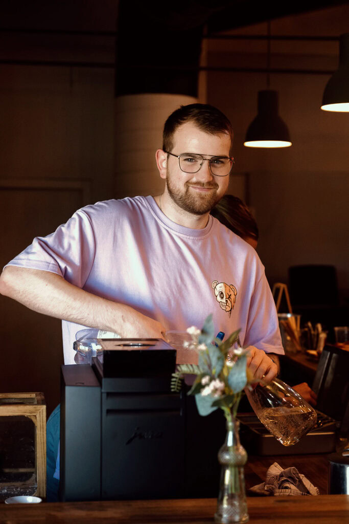 Freundlicher Barista bereitet Kaffee in einem modernen Café in Basel-Land, umgeben von warmem Licht und gemütlicher Atmosphäre.