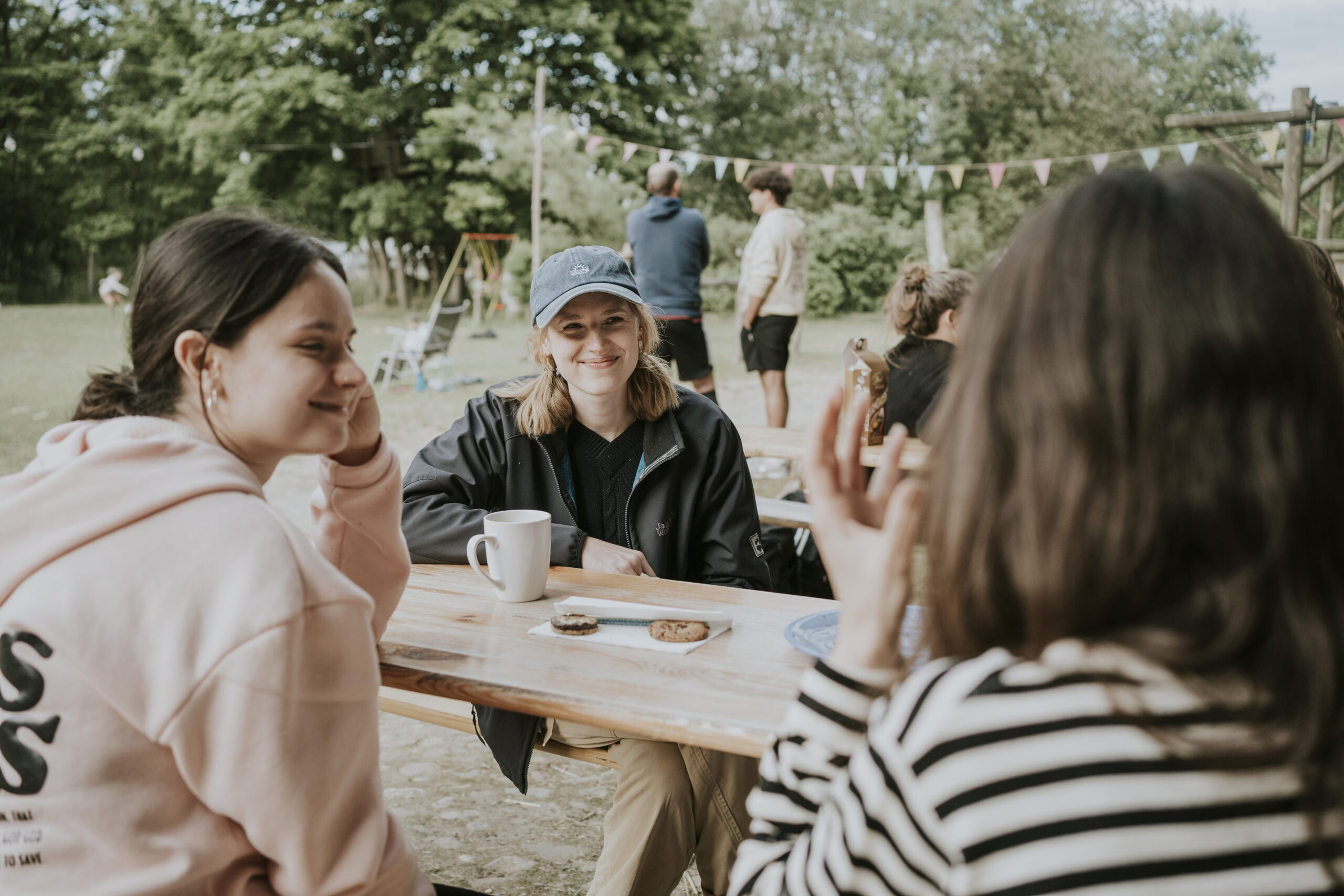 Three women are sitting at a wooden table outside, chatting.