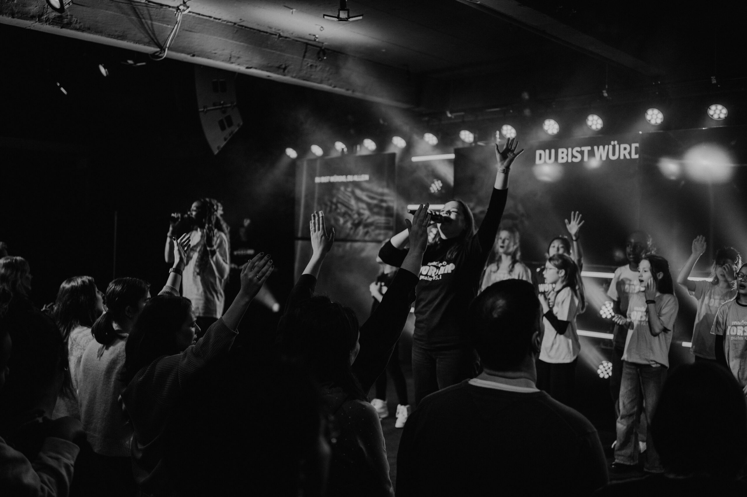People on stage singing and dancing, the audience with their hands raised.