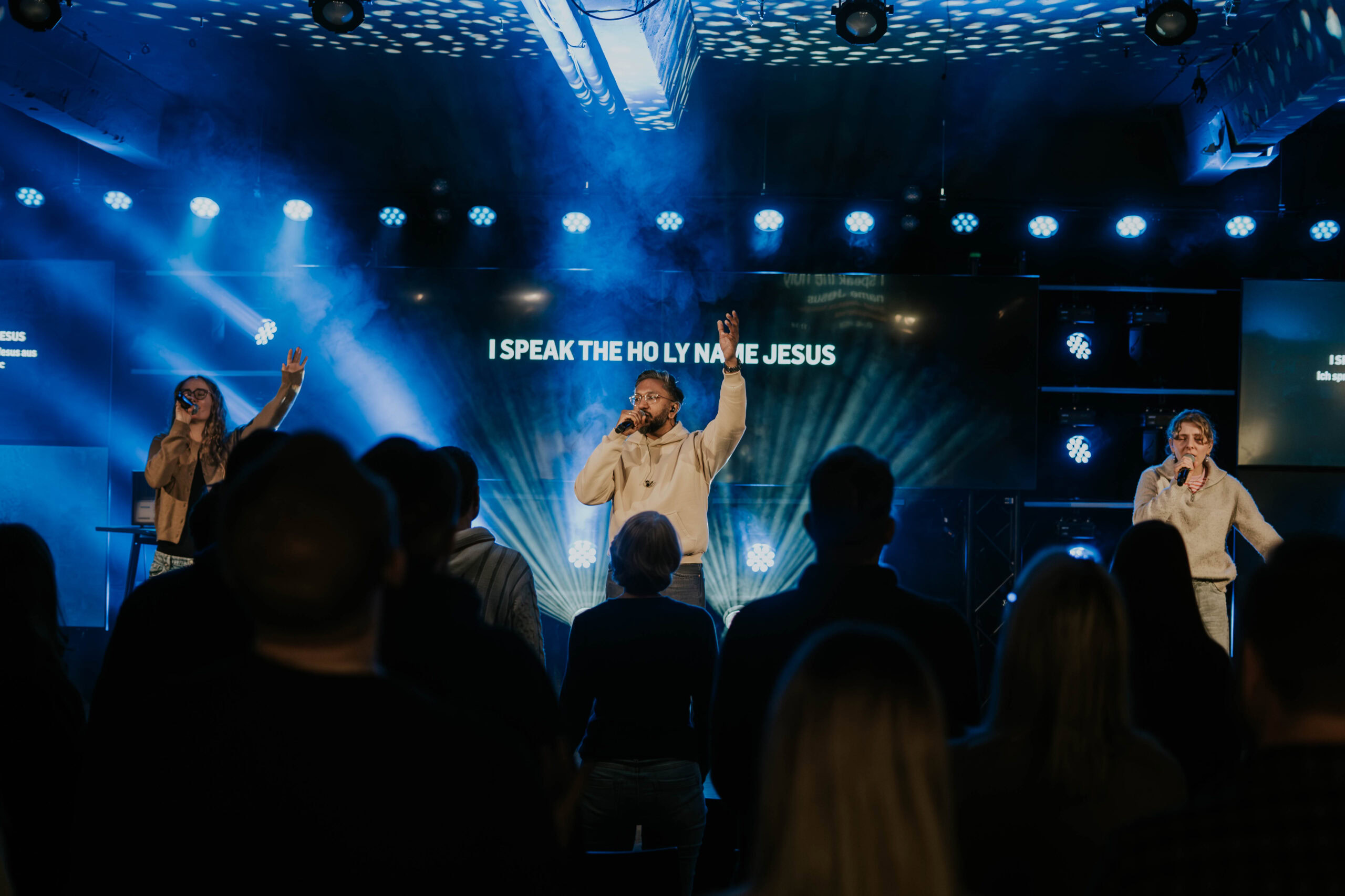 People on stage during the service, singers with microphones, lights and a projection in the background.