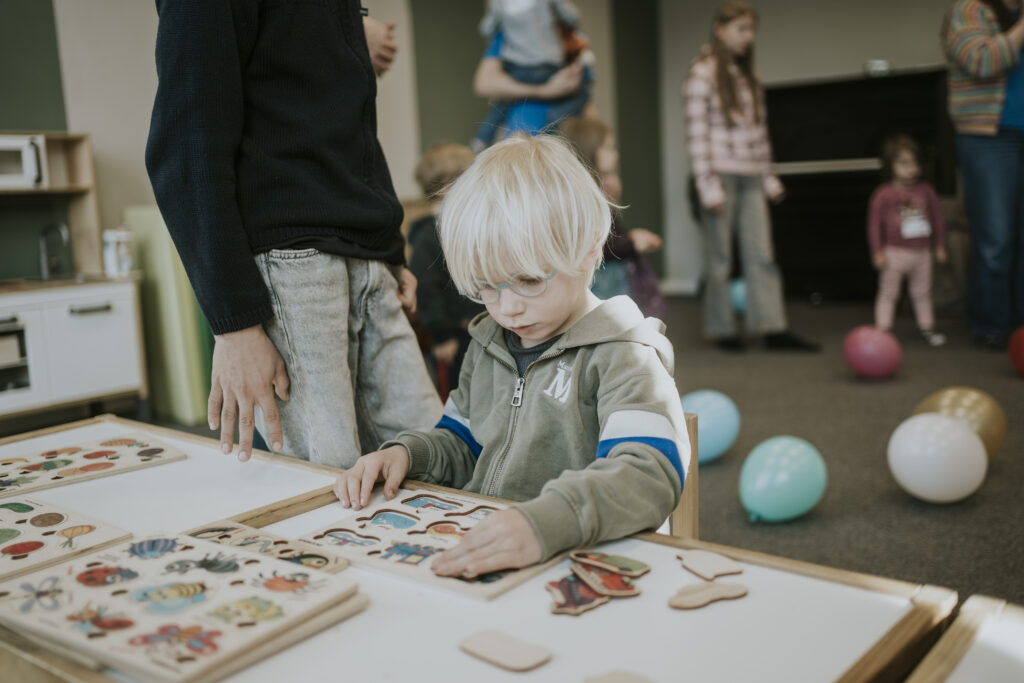 Junge Kinder spielen und lernen in einem Gemeinschaftsraum, umgeben von Spielzeug und bunten Bällen, bei einer kirchlichen Veranstaltung in Berlin.