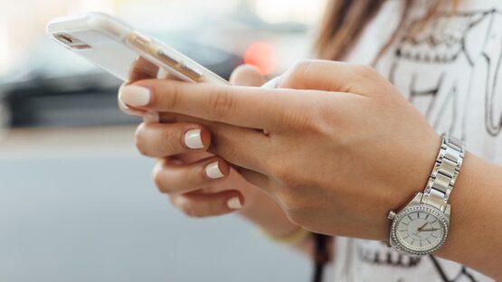 Eine Hand hält ein Smartphone, während eine andere Hand eine Armbanduhr trägt.