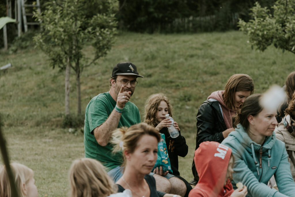 Ein Mann mit Brille, grüner T-Shirt und schwarzem Cap trinkt aus einer Flasche, umgeben von mehreren.