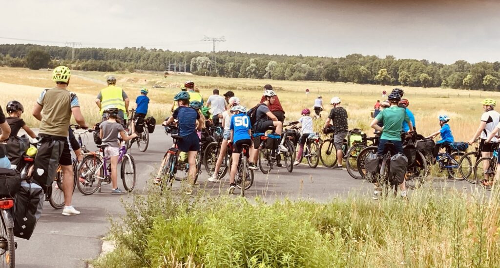 Gruppen von Radfahrern stehen auf einer Landstraße, einige mit Helmen und Rucksäcken.
