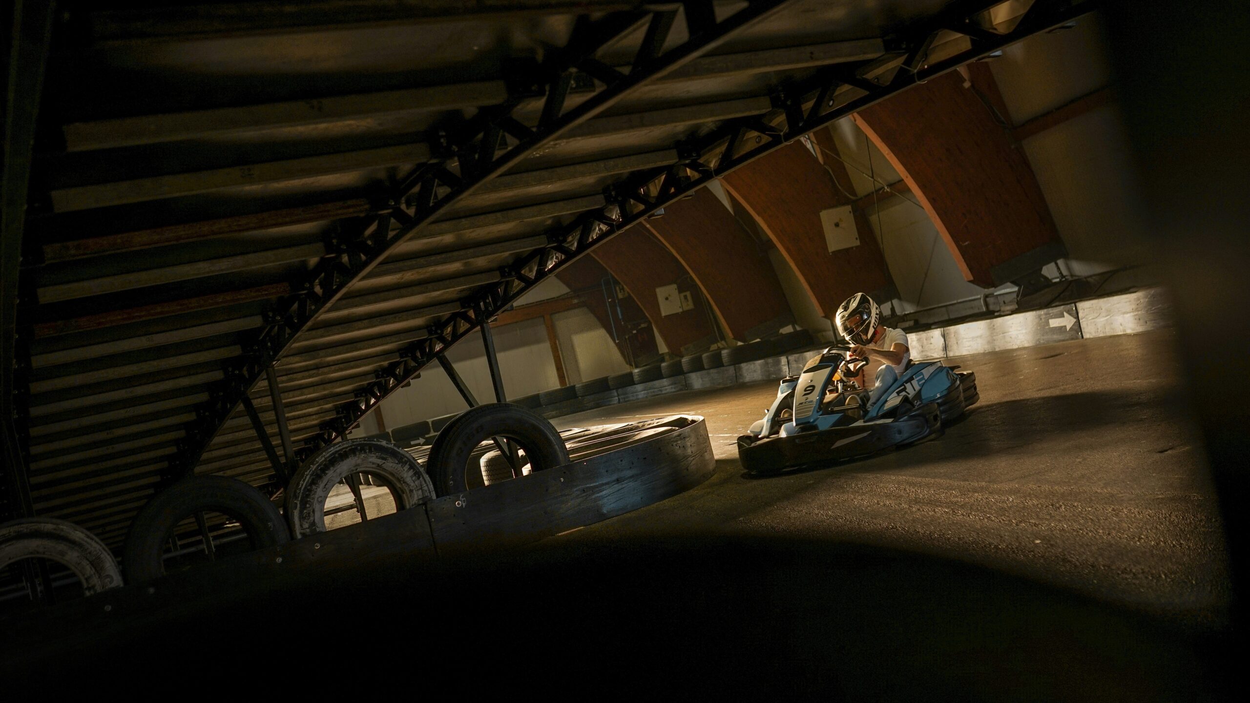 A child is driving a blue go-kart on a racetrack; tires are visible along the wall.