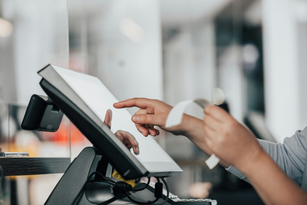 Person hält Kreditkarte vor Kassenterminal, Finger tippt auf Bildschirm.