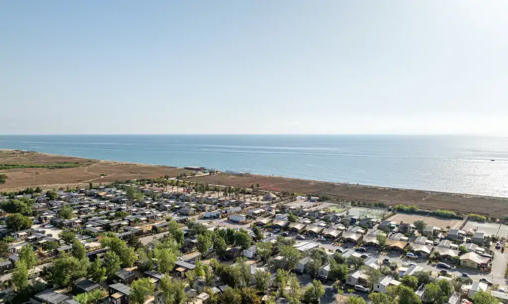 Blick auf eine Wohnsiedlung mit Häusern und Bäumen, im Hintergrund das Meer und der Himmel.