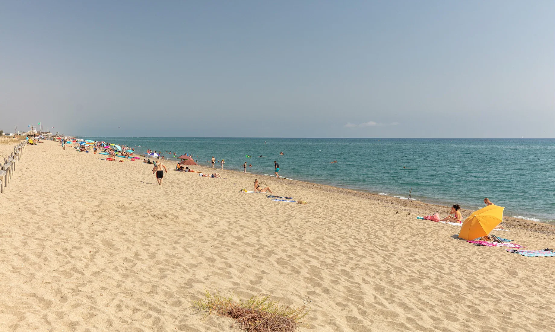 Strand mit Sonnenschirmen, Badegästen und Meer im Hintergrund.