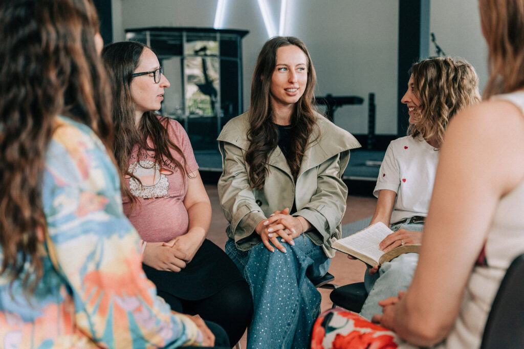Fünf Frauen sitzen im Kreis und sprechen in einem Raum.