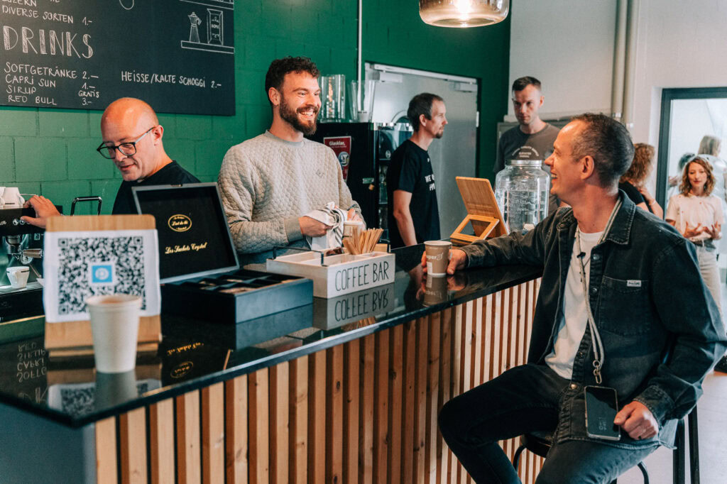 Ein Mann bestellt Kaffee an der Kaffeebar, während ein Mitarbeiter hinter dem Tresen steht. Weitere.