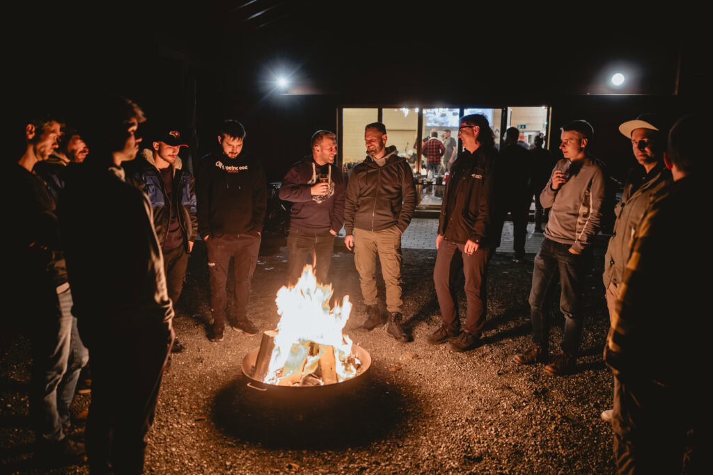 Altersgerechte Gruppen beim Lagerfeuer in der Nacht. Jugendliche und Erwachsene genießen einen entspannten Abend mit Gesprächen und Feuer.