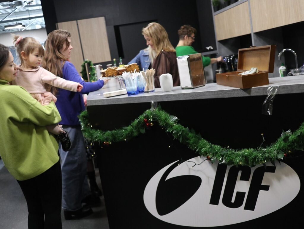 People standing at a coffee shop counter with a black and white logo reading "ICF" and green garland.