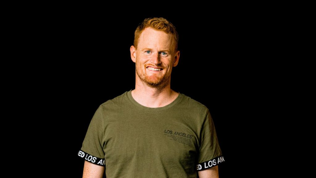 Freundlicher Gemeindeleiter bei ICF XY, der in einem grünen T-Shirt vor einem schwarzen Hintergrund steht, symbolisiert Engagement und Gemeinschaftsgeist.