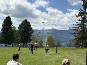 Menschen spielen auf einer Wiese, einige werfen einen Ball.