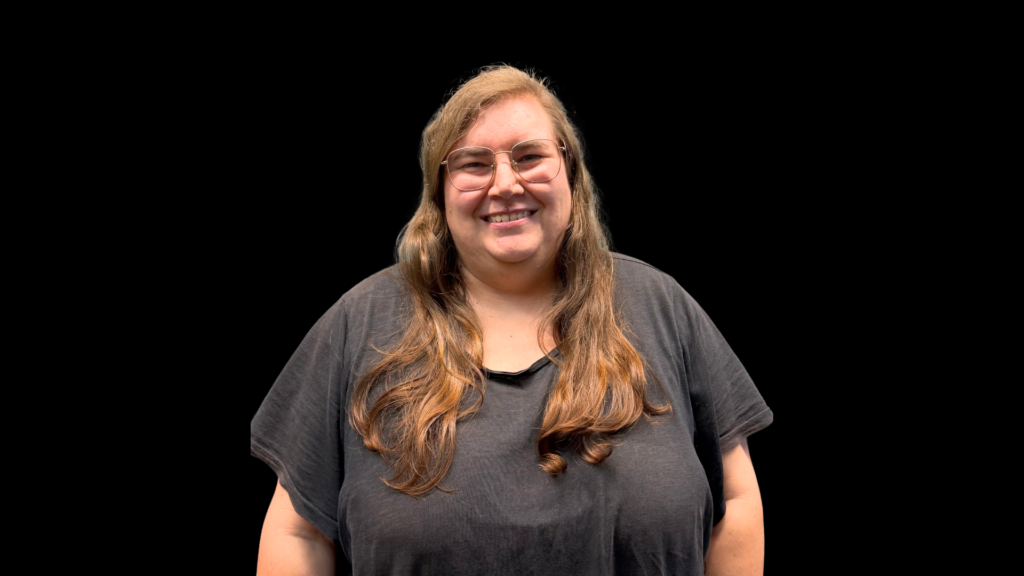Frau mit Brille, lange Haare, lächelnd, schwarzes T-Shirt.