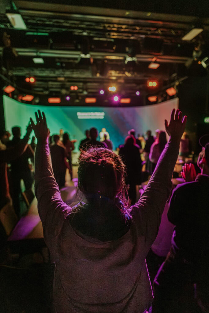 Person with raised hands in a nightclub with colorful lights.