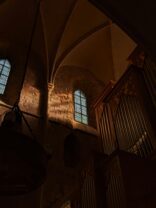 Innenansicht einer Kirche mit hohen, bunten Fenstern und Holzgeländer.