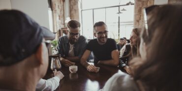 Menschen sitzen an einem Tisch in einem Café, lachen und unterhalten sich.