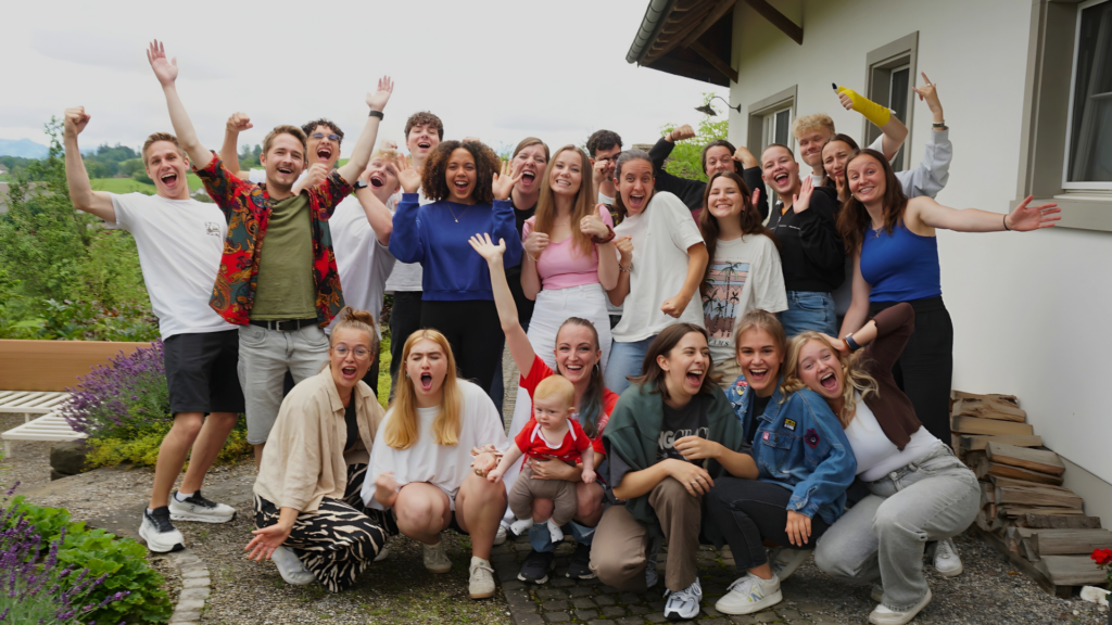 Gruppe von Menschen unterschiedlichen Alters, die draußen vor einem Haus stehen und lachen.