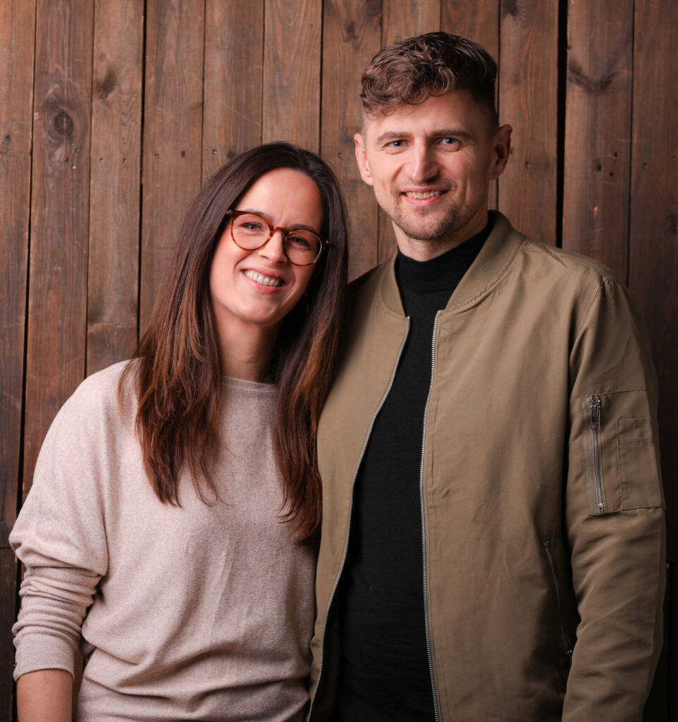 Freundliches junges Paar vor Holzwand, Menschen, Lifestyle, smiling, modern, casual, Partnerschaft, Wohlbefinden, authentisch, Lifestyle-Fotografie, urban, Freizeit, positive Energie, glücklich, Natur, Offene Haltung, Trends, jugendlich, Lifestyle-Content.