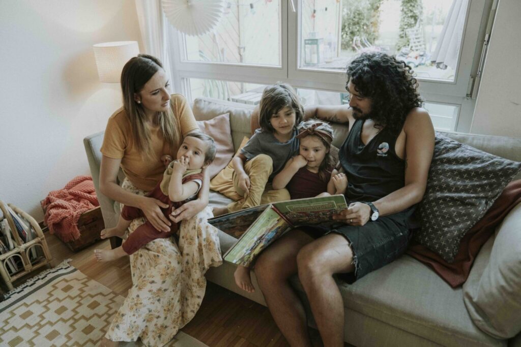 Familie liest gemeinsam ein Buch auf dem Sofa im Wohnzimmer.