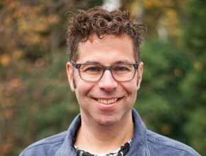 Mann mit Brille, lächelnd im Freien.