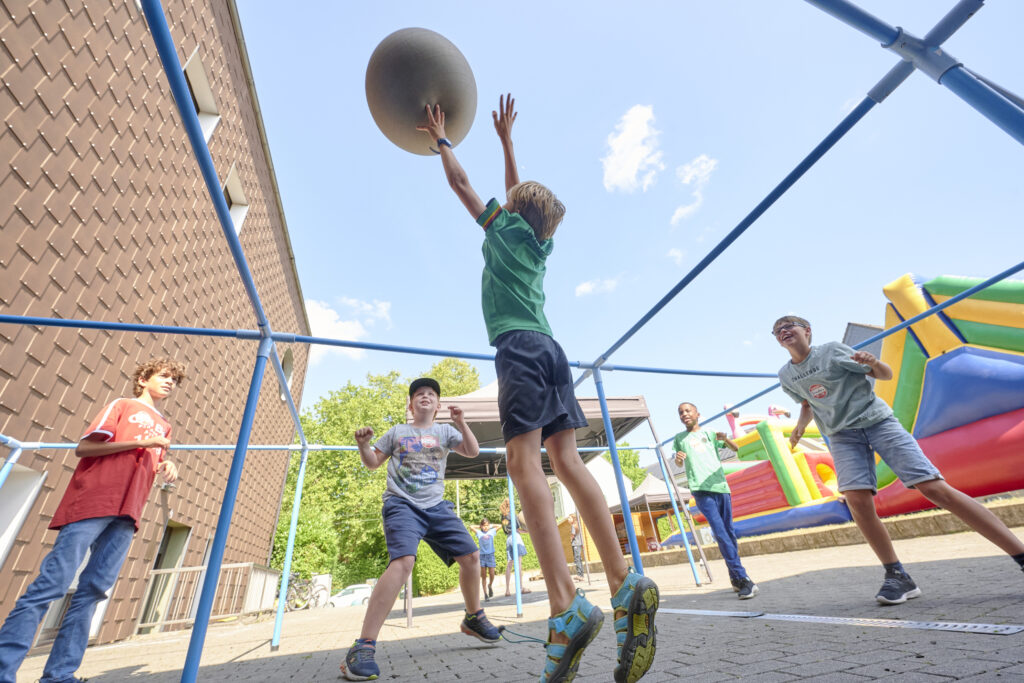 Kinder spielen lachend und aktiv beim Spiel mit Ball unter blauem Himmel bei ICF Kirche in Essen, Spaß und Gemeinschaft im Mittelpunkt.