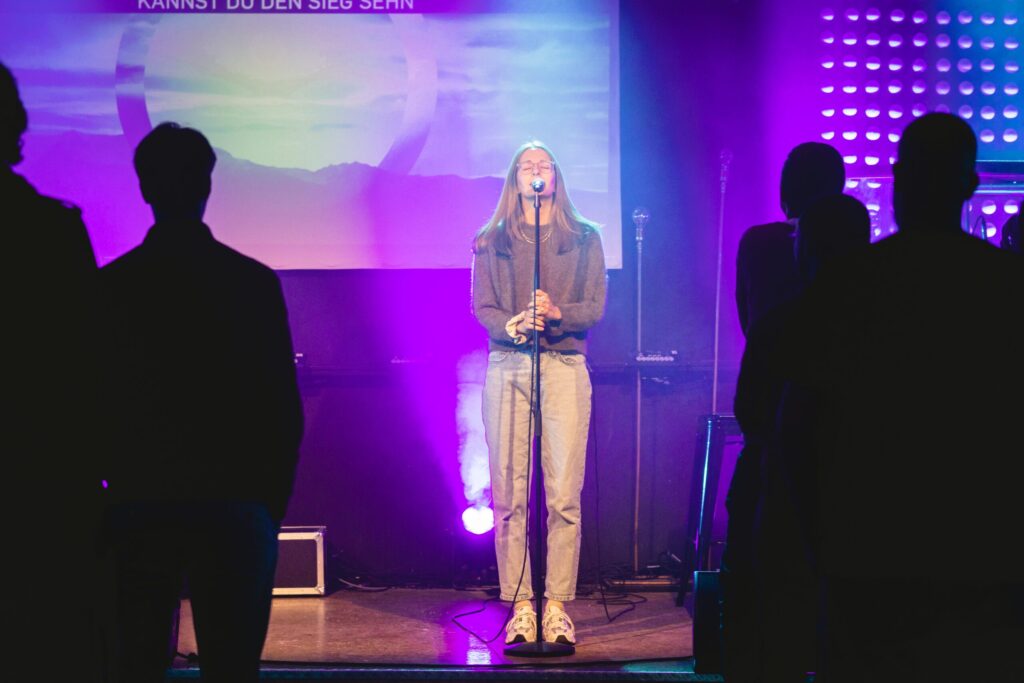 Junge Menschen beim Lobpreis bei ICF Essen, kreativ beleuchteter Raum mit Live-Musik, die Gemeinschaft und Glauben verbindet, Jugendliche und Erwachsene feiern Christentum, inspirierende Atmosphäre.
