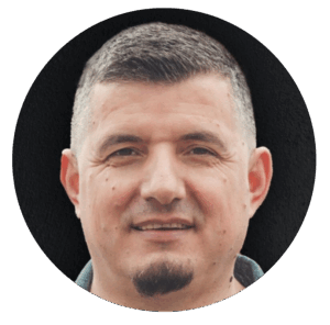 Nahaufnahme eines Mannes mit kurzen Haaren und Bart, lächelnd, vor schwarzem Hintergrund, repräsentiert einen Pastor oder Gemeindeleiter bei ICF Essen.