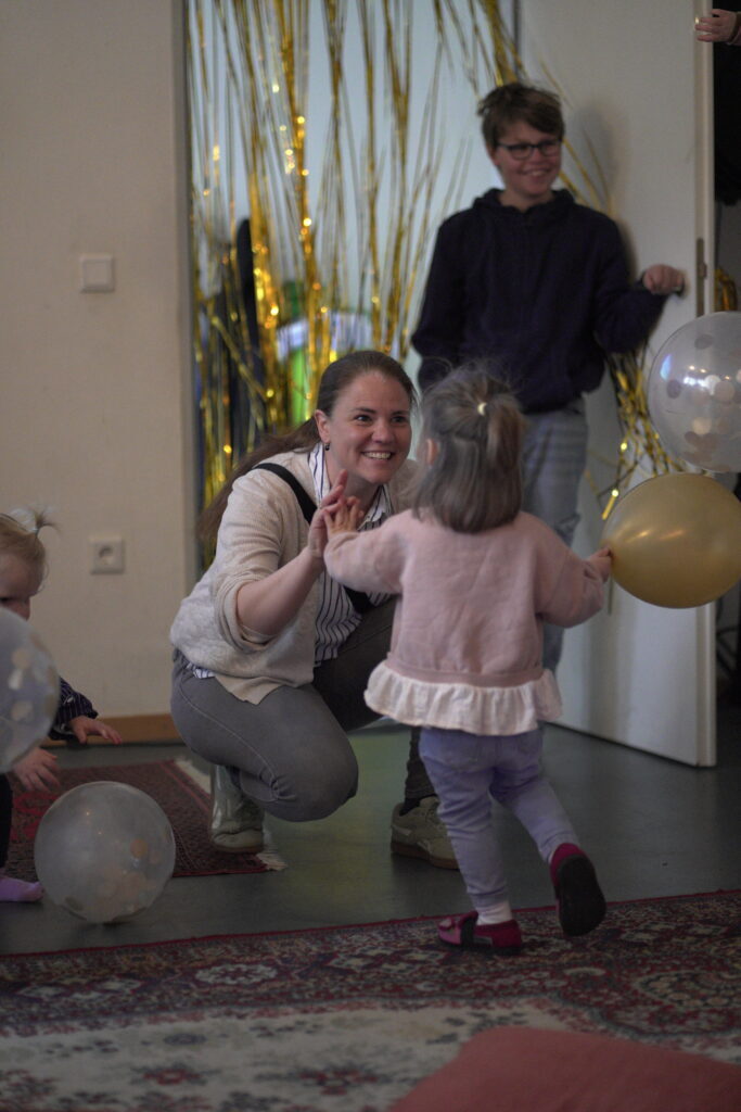 Eine Frau kniet auf dem Boden, umarmt ein kleines Mädchen, das mit Ball spielt, im Raum mit Dekorati.