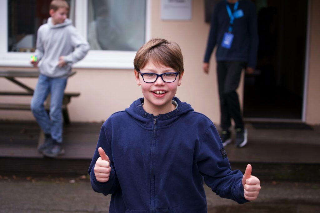 Ein Junge mit Brille und blauer Jacke zeigt Daumen nach oben.