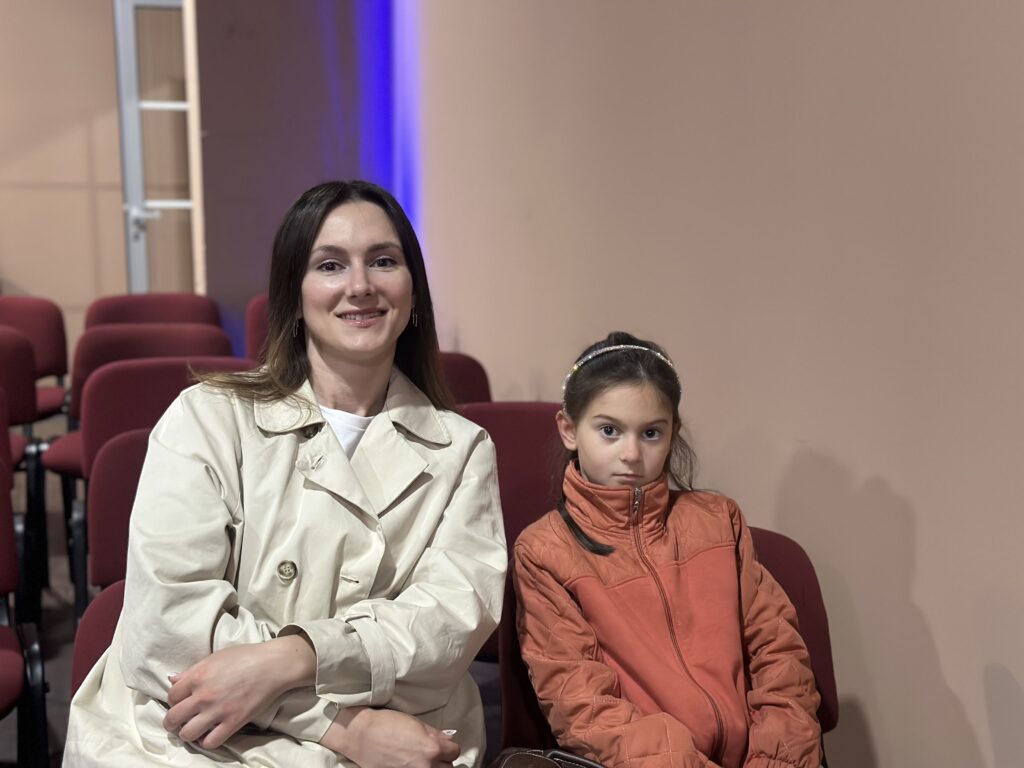 Woman and girl sitting in theater seats, facing forward, with empty seats around them.
