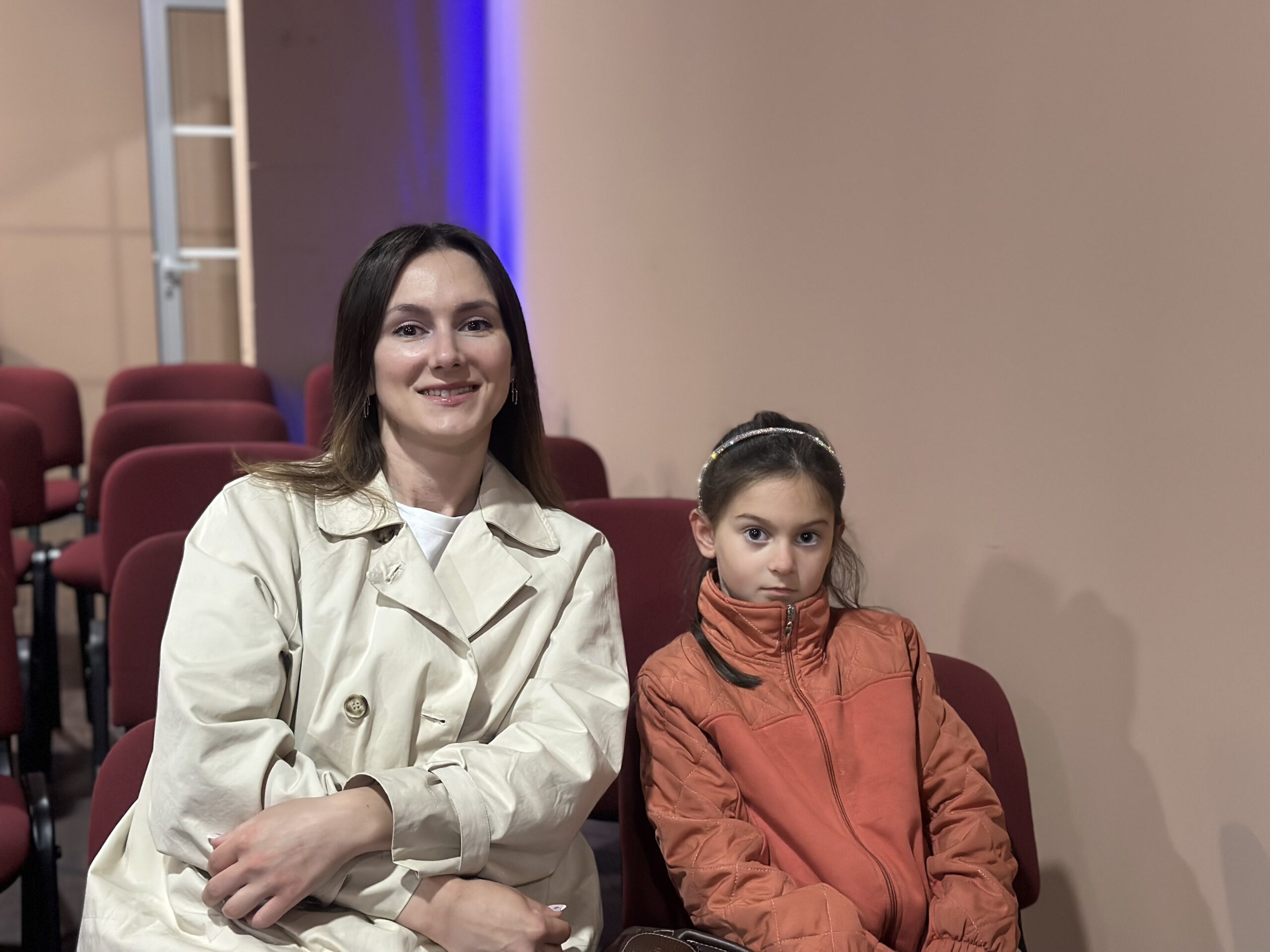 Woman and girl sitting in theater seats, facing forward, with empty seats around them.