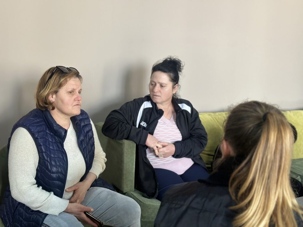 Three women sitting on a green sofa engaged in conversation.