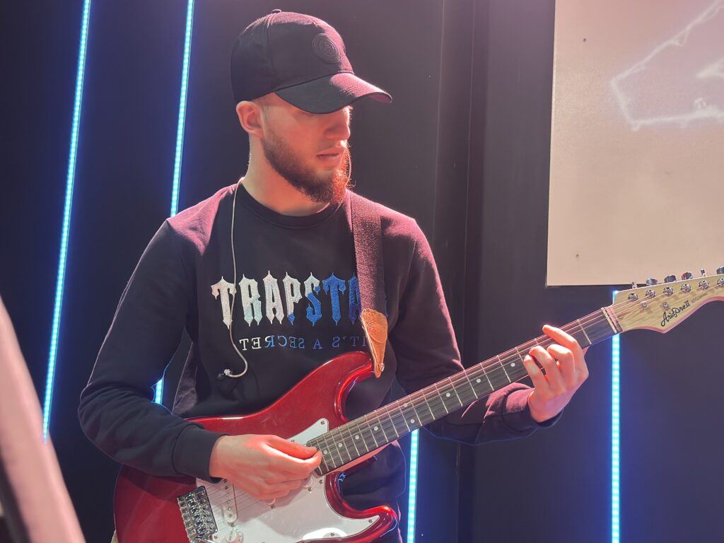 A man wearing a black cap and black sweatshirt playing a red electric guitar.