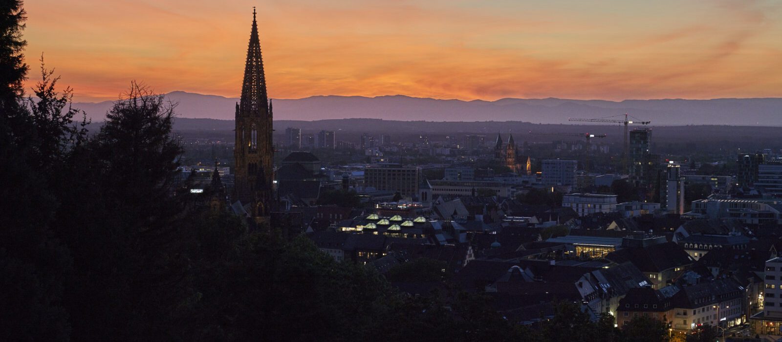 Skyline bei Sonnenuntergang mit Kirchturm im Vordergrund.