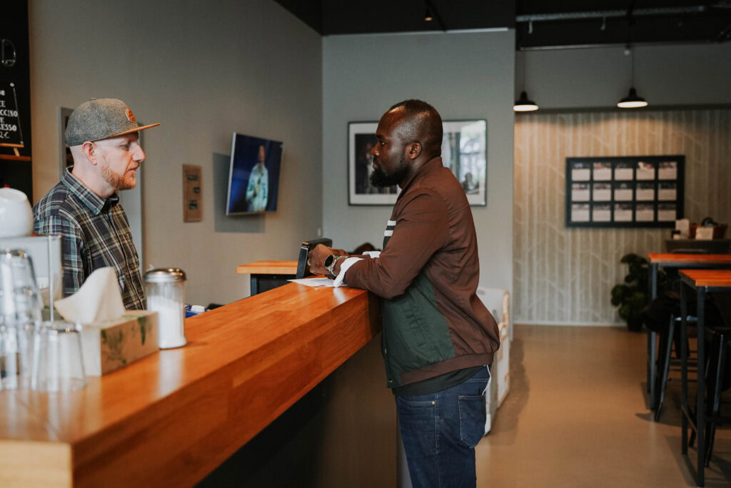Zwei Männer sprechen an der Theke eines Cafés.
