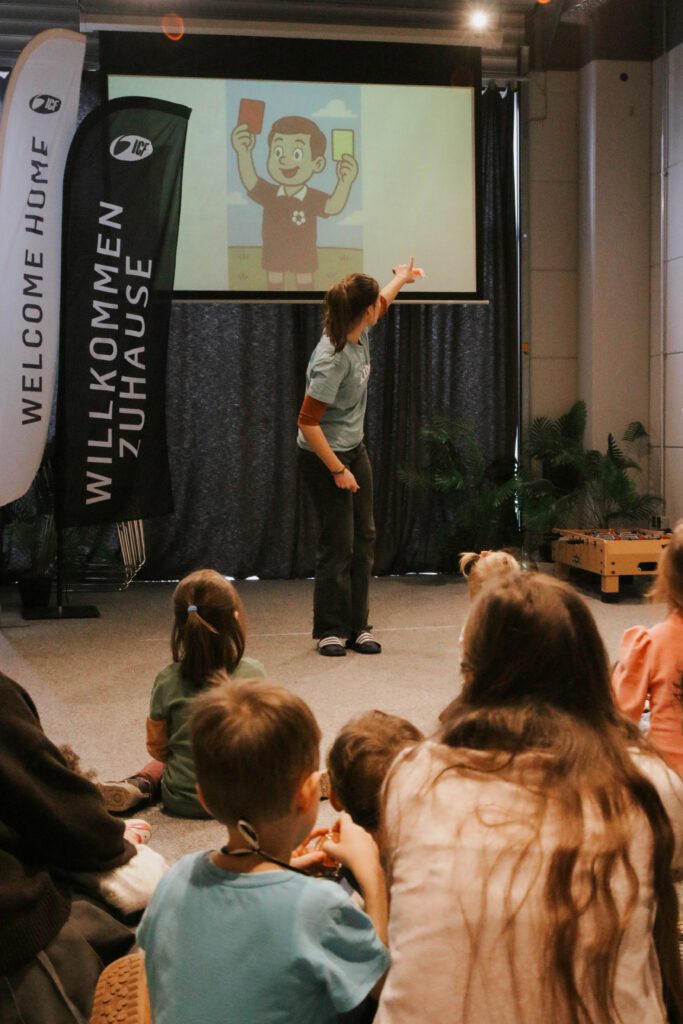 Frau zeigt auf eine digitale Illustration eines Jungen mit Smartphone vor einer Gruppe Kinder.
