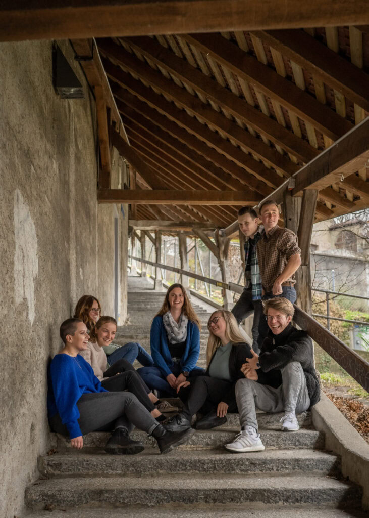 Einheimische Jugendliche sitzen entspannt auf den Treppen vor einer Kirche in Fribourg, umgeben von Natur, während sie Gemeinschaft und Glauben in einer freundlichen Atmosphäre teilen.