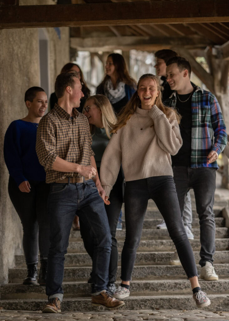 Der junge Menschenkreis beim Treffen im Freien, lachend und in Gespräche vertieft, symbolisiert Gemeinschaft und Freude in der Kirche.
